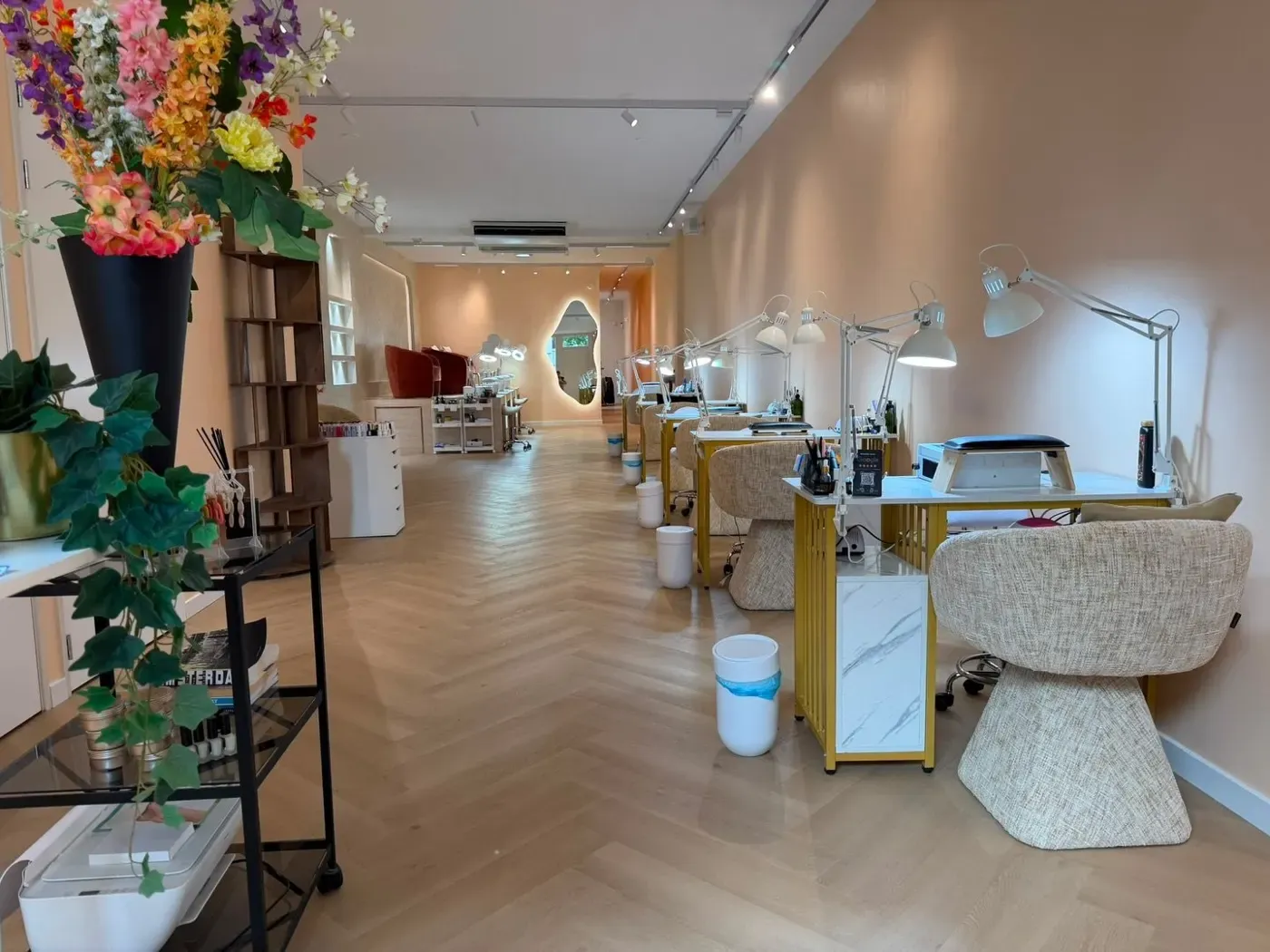 De salon van Bellamy Beauty Bar: perzikkleurige muren, visgraatvloer, gouden manicuretafels en bouclé stoelen